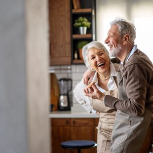 Happy senior couple communicating while having fun in the kitchen together Happy mature couple communicating while having fun in the kitchen together